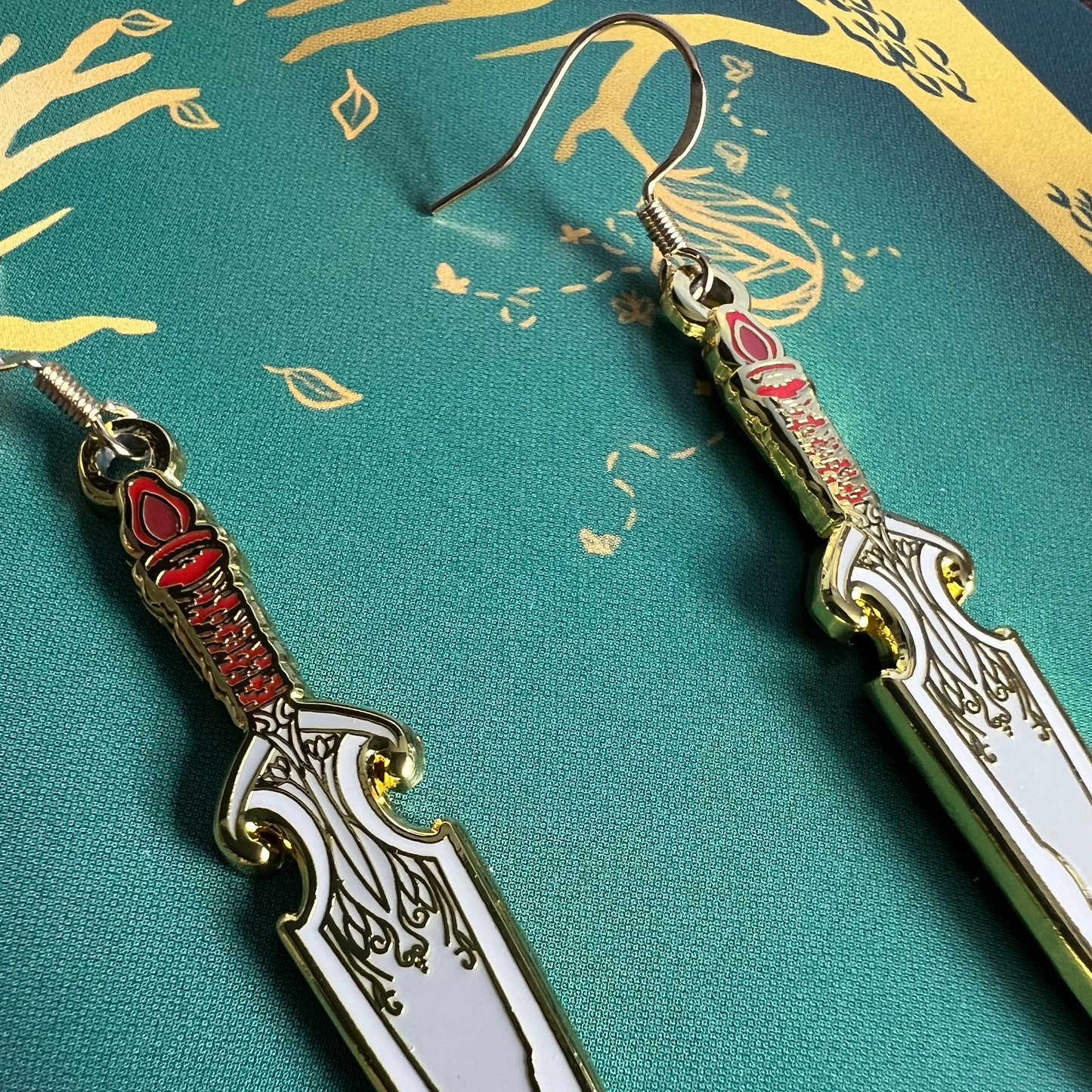 Decorative dagger-shaped earrings on a green background with gold accents.
