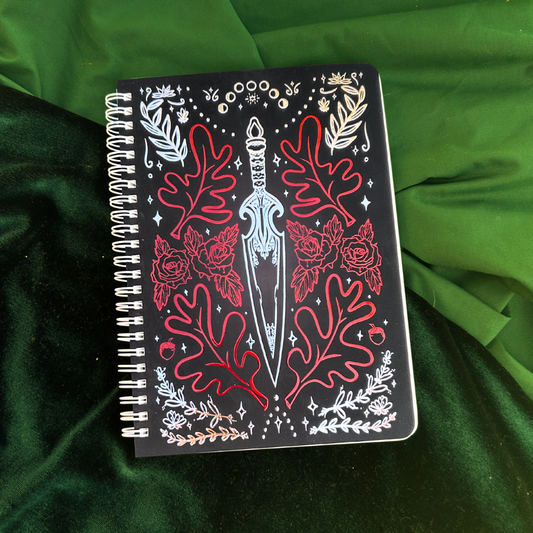 Notebook with decorative cover featuring a sword and floral designs on a green fabric background