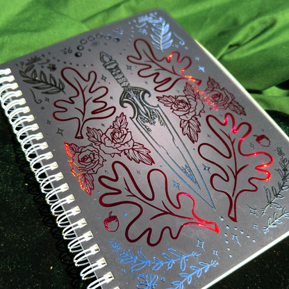 Notebook with decorative sword and leaf design on a green fabric background