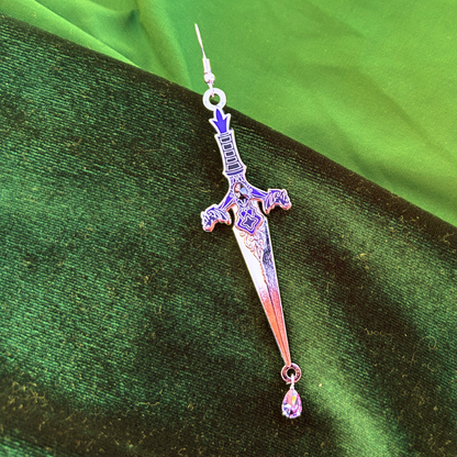 Sword-shaped earring with a teardrop pendant on a green fabric background