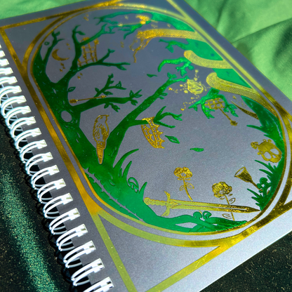 Spiral-bound notebook with decorative green and gold design on a green fabric background