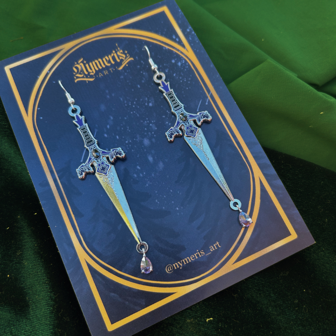 Sword-shaped earrings on a blue card with gold border, against a green fabric background.