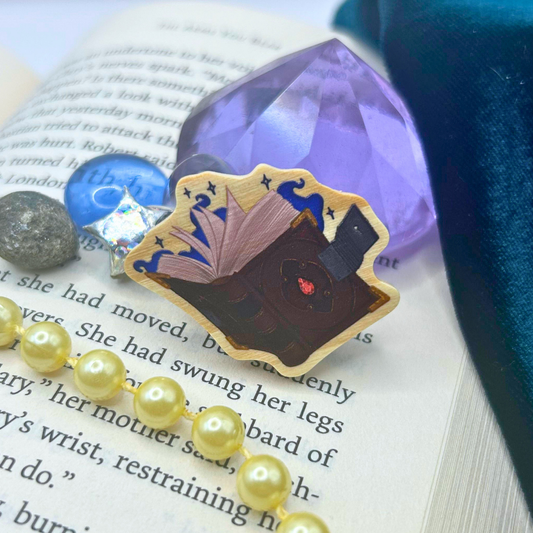 A decorative illustrated open book and dark cover, styled on an open book with purple magic and blue stones, pale yellow pearls, and a dark teal fabric background.