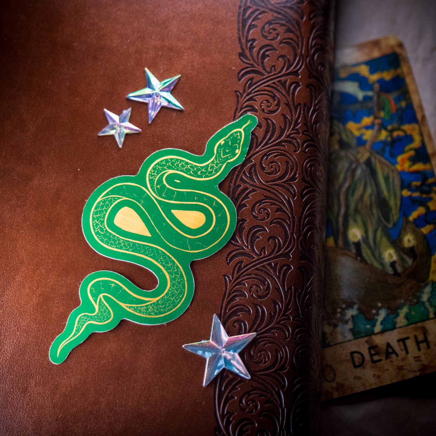 A golden green snake vinyl sticker placed on a textured brown surface, surrounded by decorative stars.